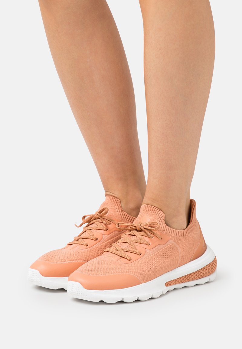 Scarpe da ginnastica color pesca con parte superiore in knit texturizzato, chiusura con lacci e suola bianca caratterizzata da un accentopuntato per grip e supporto.