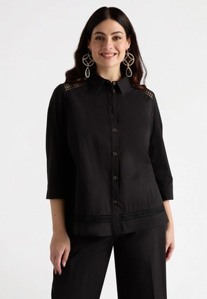 Zwarte blouse met knopen en 3/4 mouwen, met kantaccenten op de schouders en de zoom. Gemaakt van een gladde stof, gecombineerd met bijpassende broek.