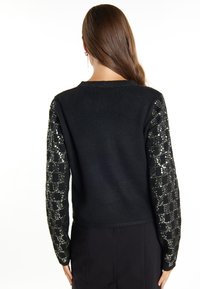 Maglione nero con un corpo testurizzato e un motivo a scacchi in paillettes sulle maniche, con scollo rotondo e polsini a costine.