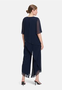 Granatowy, przezroczysty top z krótkimi rękawami nałożony na pasujące szerokie spodnie. Posiada drapowanie z przodu oraz zamek błyskawiczny na dekolcie z tyłu.