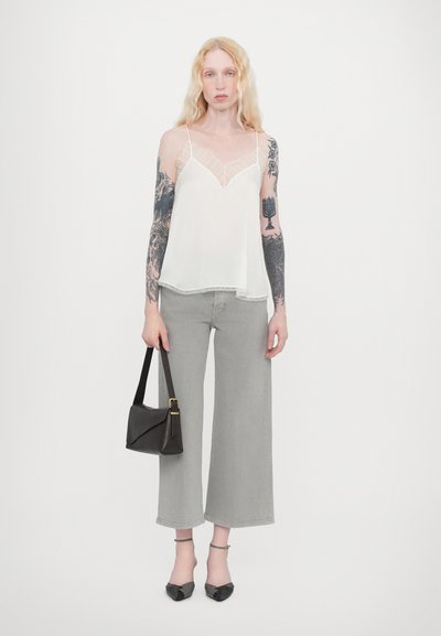 Camisole blanche transparente avec bordure en dentelle, jeans gris à jambes larges, sac à main noir avec des accents dorés, et escarpins noirs à bout pointu.
