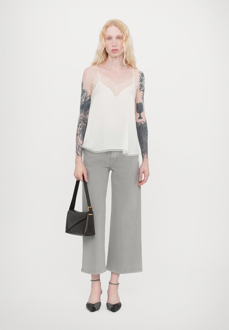 White sheer camisole with lace trim, grey wide-leg jeans, black handbag with gold accents, and black pointed-toe heels.