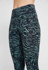 Högmidjade leggings med ett zebramönster i turkos och svart, tillverkade av stretchigt material med mjuk textur och platta sömmar.