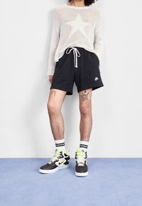 Vitt stickat tröja med ett stort stjärnmönster, svarta shorts och flerfärgade Nike högskor med neonlysande detaljer.