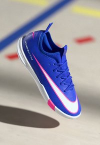 Modrá sportovní obuv s texturovaným svrškem, která má bílý a růžový design swoosh, štíhlý tvar a kontrastní bílou podrážku.