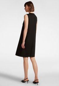 Abito nero senza maniche con una silohuette A-line morbida, texture liscia, lunghezza ginocchio e scollatura semplice. Indossato con sandali neri con tacco.