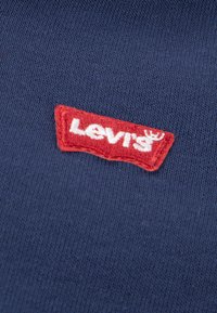 Κόκκινο λογότυπο Levi's ραμμένο σε σκούρο μπλε πλεκτό ύφασμα.