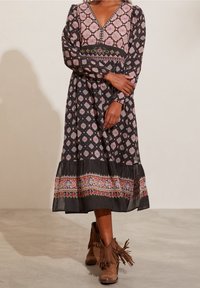 Kvinna iklädd en mönstrad långärmad midiklänning med blommiga och geometriska mönster, ihopparad med bruna boots med fransar.