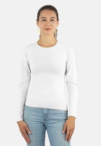 Weißes, langärmliges Shirt mit rundem Ausschnitt, aus glattem Stoff, kombiniert mit hellblauen Jeans. Das Modell steht frontal.