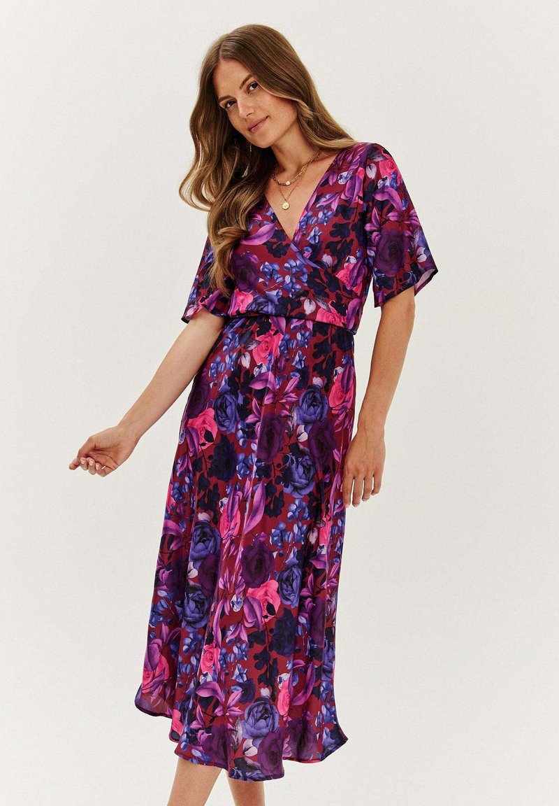 Kwiatowa sukienka wrap z krótkimi rękawami, z fioletowymi, różowymi i niebieskimi kwiatami na ciemnym tle. Lekka, zwiewna tkanina z dekoltem w kształcie litery V.