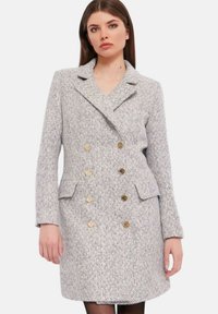 Cappotto grigio a doppio petto in tweed con bottoni dorati, revers a punta, tasche a pattina e vestibilità sartoriale. Texture liscia e forma strutturata.