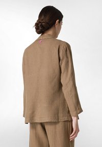 Ruskea pellavapuku, jossa on rento istuvuus, takana vaaleanpunainen yksityiskohta, pitkät hihat ja yksinkertainen kaulussuunnittelu.