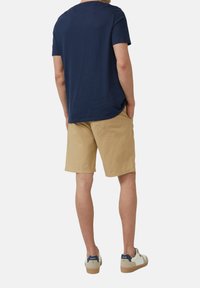 Marineblaues Rundhals-T-Shirt, khakifarbene Shorts und weiße Sneakers mit Marineblau-Details. Die Shorts sind über dem Knie, haben eine lässige Passform und eine einzelne Gesäßtasche.