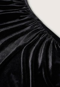 Tissu en velours noir avec une texture froncée, présentant une douce brillance et un drapé fluide. Le matériau a une apparence lisse et riche.