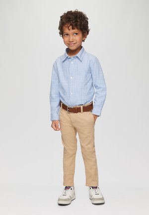 Gestreept blauw overhemd met lange mouwen, beige broek, bruine riem en witte sneakers. Het overhemd heeft knopen en een losse pasvorm.