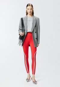 Blazer a quadri grigi su una T-shirt grigia, abbinato a leggings rossi aderenti con strisce bianche ai lati e ballerine metalliche con punta.