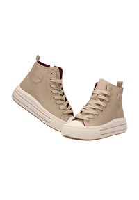 Zapatillas altas de color beige hechas de cuero suave con una suela de goma blanca, que cuentan con un parche de logo redondo y cordones de color beige.