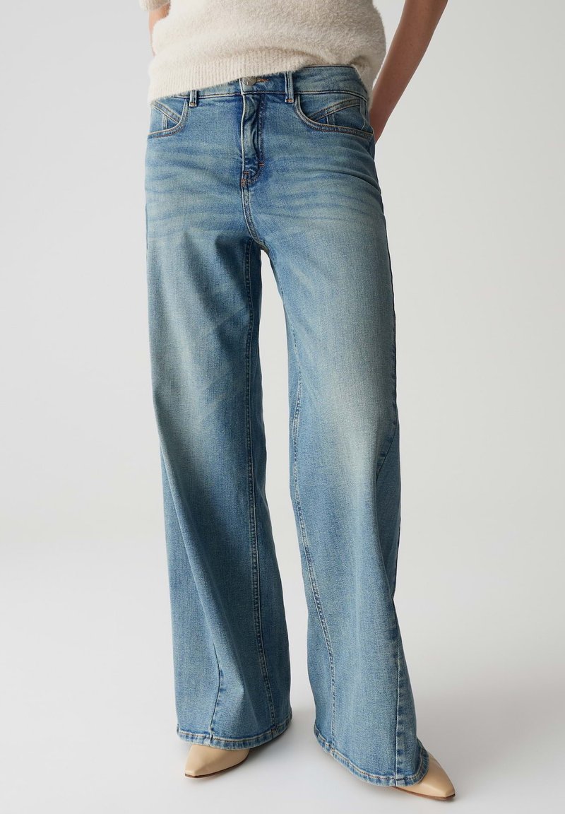 Jeans a gamba larga di colore blu chiaro realizzati in denim, con una finitura sbiadita, design a cinque tasche e dettagli di cucitura sottili sulla vita.