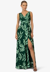 Robe maxi verte avec un motif de feuilles, décolleté en V, corsage drapé et fente sur le côté. Fabriquée en tissu léger avec une texture douce.