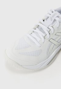 Baskets de sport blanches avec un dessus en mesh et synthétique, des accents texturés, un laçage, et des détails réfléchissants sur le côté.
