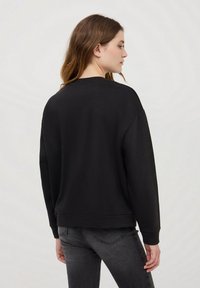 Czarna bluza z luźnym krojem, okrągłym dekoltem i ściągaczami na rękawach, wyeksponowana od tyłu na jasnoszarym tle.