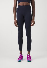 Leggings blu navy con vita alta, caratterizzati da pannelli laterali neri a contrasto e tessuto liscio. Abbinati a scarpe da ginnastica rosa brillante.