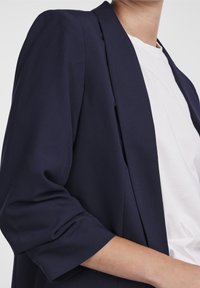 Marinblå blazer med avslappnad passform och trekvartslånga ärmar. Tillverkad av ett slätt tyg, har en strömlinjeformad design och öppen front.