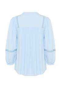 Gaiši zila blūze ar pūkainām piedurknēm, teksturēta audi, izšūtas detaļas uz pleciem un brīva piegriezuma. Skats no aizmugures.