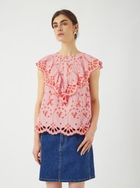 Top rosa con maniche a volant, caratterizzato da intricati ricami arancioni e orlo ondulato. Abbinato a una gonna di jeans blu.