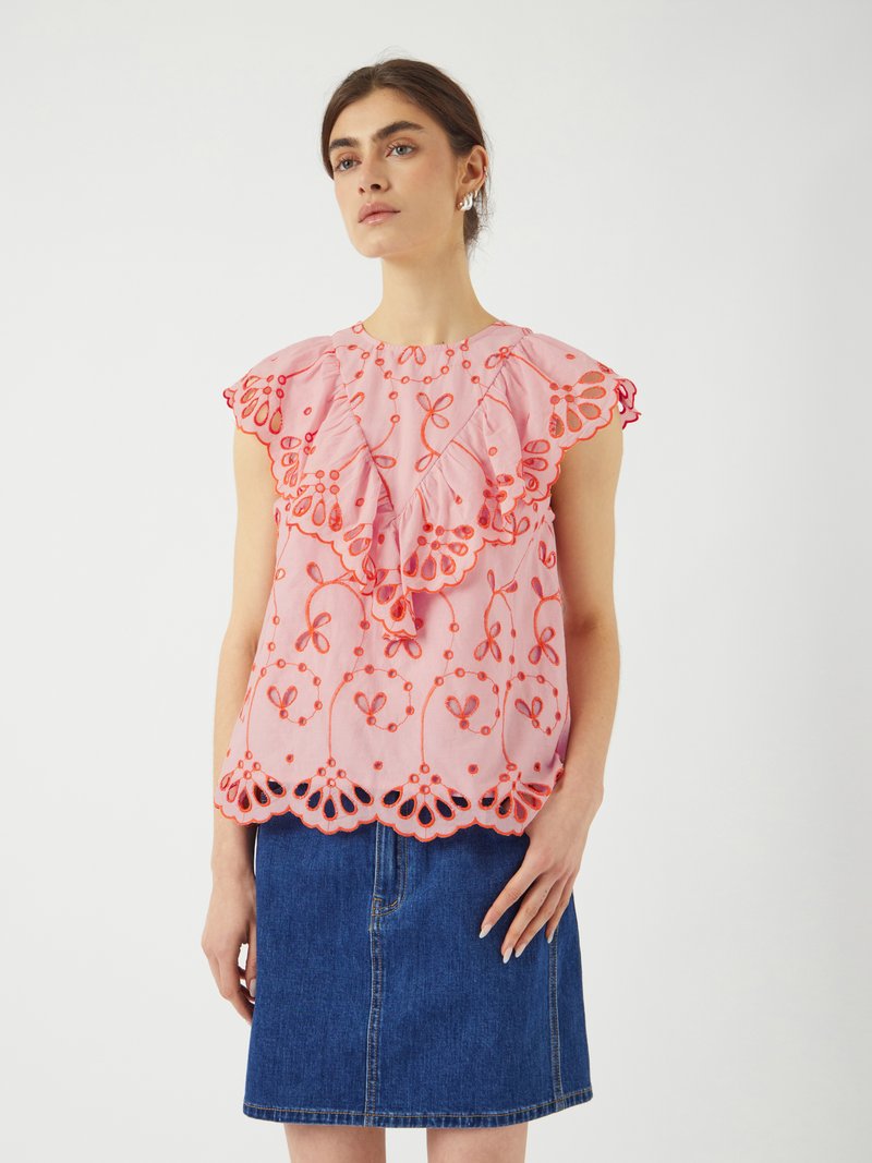 Top rosa con maniche a volant, caratterizzato da intricati ricami arancioni e orlo ondulato. Abbinato a una gonna di jeans blu.