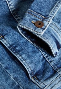 Giacca di denim in blu sbiadito, con chiusura a bottoni robusta e dettagli di cucitura visibili. Texture morbida con un design classico del colletto.