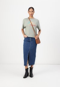 Green cropped t-shirt with "Cow Girls" graphic, blue denim maxi skirt with front slit, and black ankle boots. Brown crossbody bag.