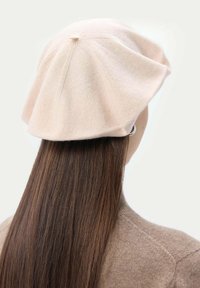 Rosa ullberet med en rund, mjuk form. Har en central söm och en lös passform som täcker baksidan av huvudet. Slät textur.