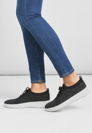 Schwarze gestrickte Sneaker mit strukturiertem Obermaterial, weißer Sohle und Schnürdesign, kombiniert mit verkürzten blauen Jeans.