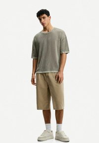 Light green ribbed short-sleeve shirt paired with beige knee-length shorts; model wearing cream-colored sneakers and white socks, standing upright.