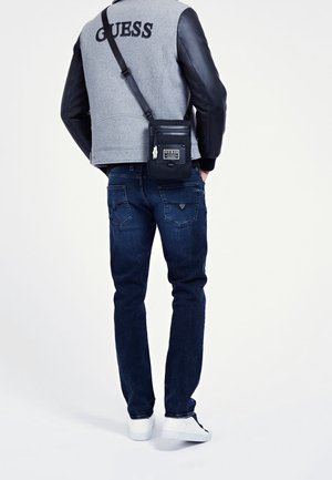 Veste en polaire grise avec des manches en cuir noir, jean en denim bleu et sac bandoulière noir. Des baskets blanches complètent l'ensemble.