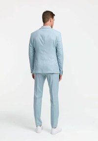 Helles blaues Anzug aus glattem Stoff, mit schlankem Schnitt und einer Rückenöffnung, kombiniert mit weißen Sneakers.