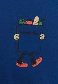 Tejido azul con un personaje de dibujos animados sosteniendo un libro con el texto "¡Revolución!", adornado con verduras y usando zuecos rojos.
