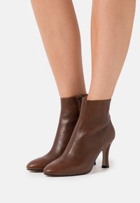 Brune læderankelstøvler med spids tå, slank hæl og lynlåsdetalje i siden. Glat tekstur og tætsiddende design.