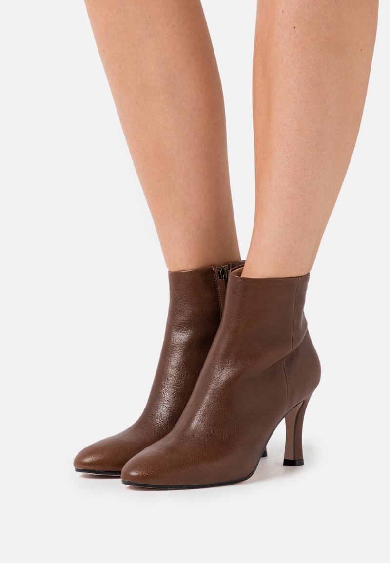 Brune læderankelstøvler med spids tå, slank hæl og lynlåsdetalje i siden. Glat tekstur og tætsiddende design.