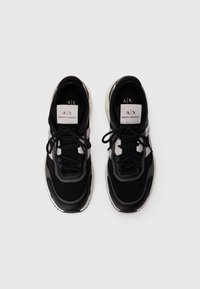 O pereche de adidași Armani Exchange în alb și negru, cu șireturile legate, văzuți de sus pe un fundal alb simplu.