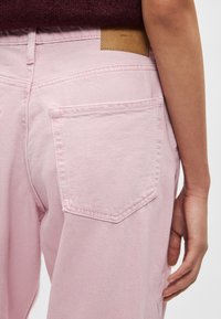 Gaisni rozā džinsi ar divām aizmugures kabatām, smalku šuvumu un tumši brūnu ādas uzlīmi pie vidukļa. Kokvilnas džinsa audums ar gludu faktūru.