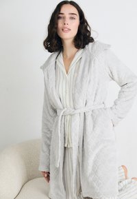 Rochie de baie gri deschis, căptușită, cu glugă, curea de legare și mâneci lungi, peste un set de pijamale cu dungi. Textură moale și detalii ale modelului vizibile.