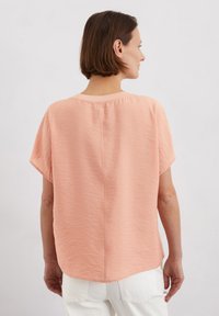 Haut court en corail clair à manches courtes, au style décontracté, en tissu texturé, avec un col arrondi et un détail de couture dans le dos. Drapé doux avec un ourlet courbé.