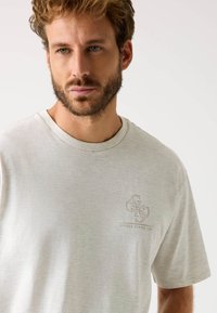 Lys grå bomulds t-shirt med rund halsudskæring og korte ærmer. Har et diskret logo-print på venstre bryst i en mørkere nuance.