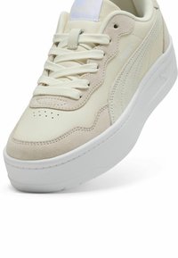 Baskets beige clair avec un dessus en cuir lisse et en daim, présentant une épaisse semelle blanche, un bout arrondi et un logo PUMA bien visible.