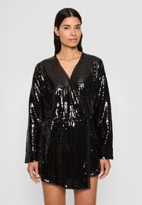Melna spīdīga sequin apkakles kleita ar garām piedurknēm, V veida kakla izgriezumu un jostu vidukļa līmenī. Audumam ir spīdīga, atstarojoša tekstūra.