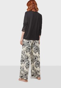 Haut noir à manches longues avec des détails en dentelle aux manches, associé à un pantalon large beige avec un motif floral noir et des hiboux.