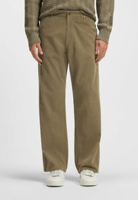Pantaloni in velluto a coste verde oliva con design a gamba dritta, dotati di tasche anteriori, passanti per cintura e zip, abbinati a sneakers bianche.
