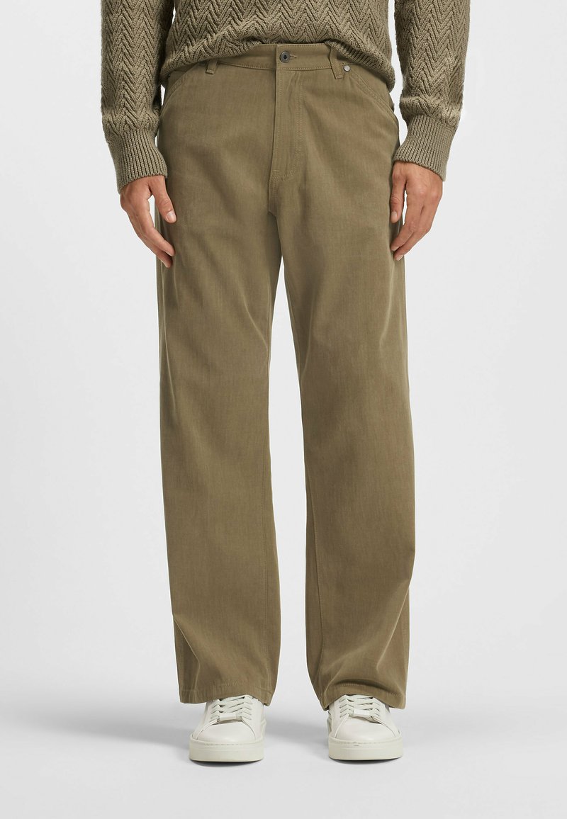 Olijfgroene ribfluwelen broek met een rechte pasvorm, uitgerust met steekzakken, riemlussen en een rits, gecombineerd met witte sneakers.